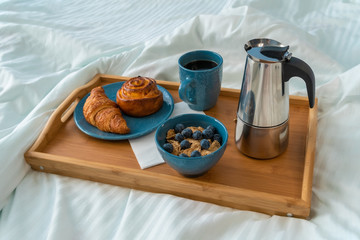 Breakfast in bed with espresso and croissant on wooden tray