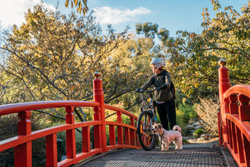 19/4/2020 Asian woman with a bike looking the view with a dog in autumn at the Botanic garden, Oamaru, New Zealand. Concept about exercise while social isolation from Coronavirus or Covid 19.