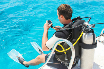 Happy scuba diver with equipment and camera is preparing for his diving lesson in the blue sea