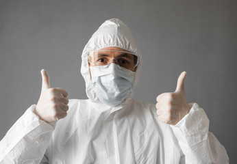 Doctor in white protective suit, medical mask and rubber gloves is showing a thumb up. Helping a people while coronavirus pandemic threat. Epidemic, pandemic of coronavirus covid 19.