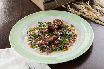 Asian cabbage salad with roast beef and sesame seeds on wooden table
