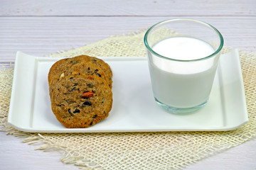 Homemade soft and chewy chocolate chip cookies and a glass of milk on white wooden table.