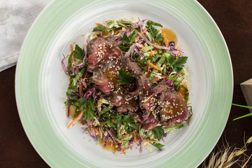 Asian cabbage salad with roast beef and sesame seeds on wooden table