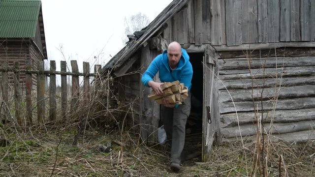 Man carries out of the old barn firewood. The old village in the Russian province.