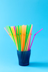Colorful plastic drinking straws in glass container on light blue background. Plastic recycling...