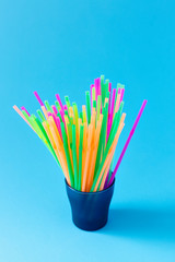 Colorful plastic drinking straws in glass container on light blue background. Plastic recycling...