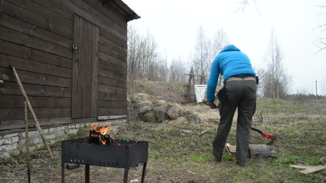 Man brings firewood from birch and kindles a fire in a brazier. 