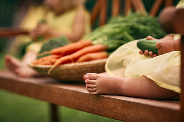 Little baby feet close up. A basket of carrots in the distance.Healthy food, green vegetarian food.