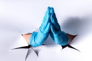 Female hand from a hole in a paper wall, in blue medical gloves