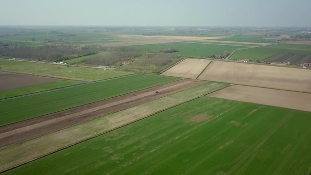 Aerial drone shot of flying up over the big wide farm fields with the tractor moving to plow the ground.