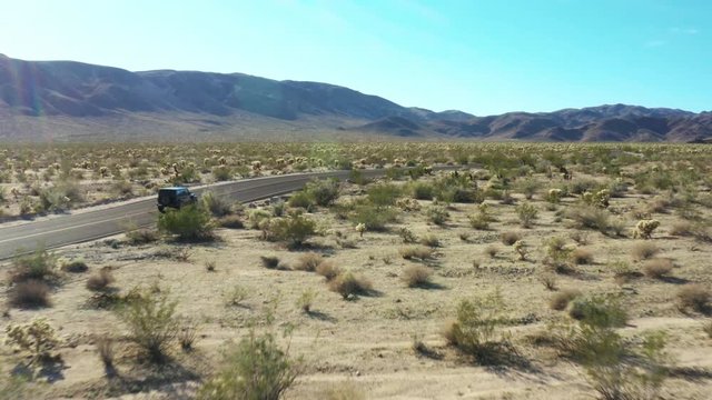 Aerial: Black Jeep driving down an empty desert dirt road in Joshua Tree.