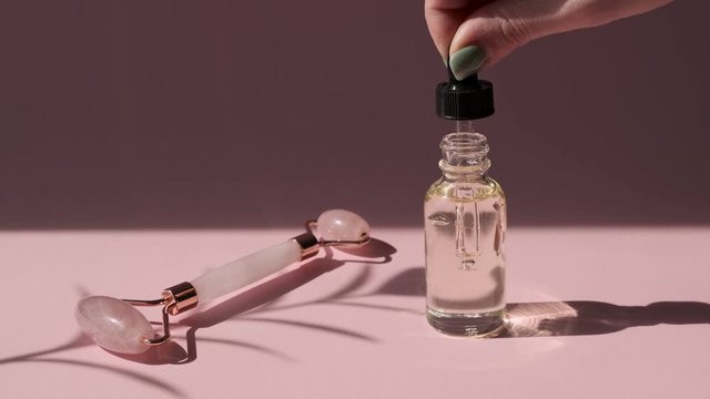 Skin care essence oil dropper glass bottle with massage quartz roller for  face of pink natural nephritis. Hydrating serum, vitamin for face skin.