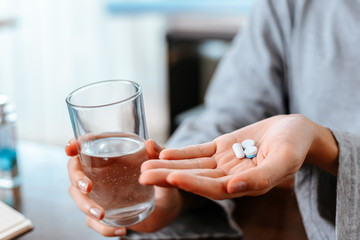 Businesswomen working at home with glass of water takes white round pill in hand.