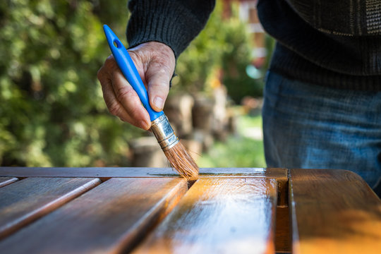 Craftsman painting wooden table. Senior man restoring of garden furniture