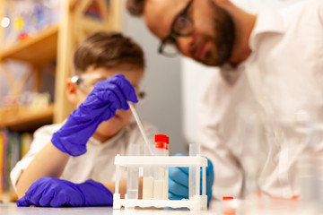 dad and son the child stayed at home conduct experiments on a white table, behind them on the wall is a white Board magnetic-marker