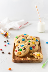 Cookies with colorful candies and chocolate chips and a bottle of milk on white background. Side view. Multicolor biscuits for holidays. Bakery