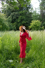 Obraz premium Girl in a red dress and hat on a background of nature.