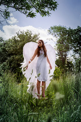 A beautiful girl with long hair in the image of an angel with white wings is soaring above the...