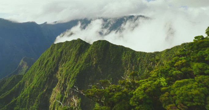 Cinematic aerial view flying over lush green misty mountain peaks in Hawaii