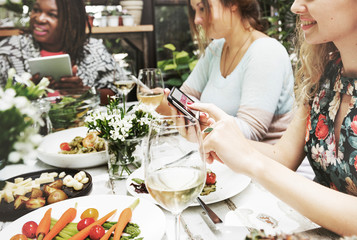 Group of diverse women having meal together using digital devices