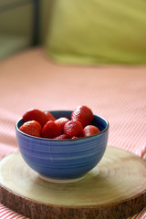 Bowl of fresh strawberries on a bed with striped sheets. Selective focus.