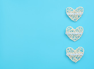 White rattan hearts with ribbon with flowers on blue background.  Mother’s day, Valentine’s day, Wedding, Birthday or other suitable event celebration card concept. Flat lay with copy space for text.