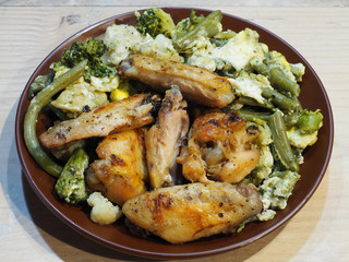 Grilled chicken wings, green string beans, cauliflower and broccoli with fried egg in a brown plate on a light wooden background. Traditional meat dish with vegetables for lunch closeup, top view