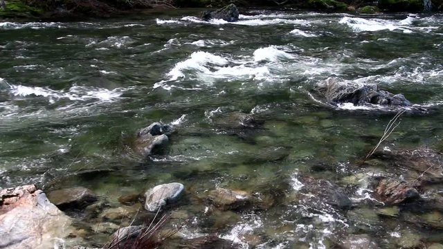 Left to right pan along a very clearn, fast moving wild and scenic river in Southern Oregon with granite boulder outcroppings and river bed