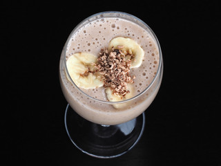 Milkshake with banana slices and chocolate in a glass wine closeup on a black background, top view. Natural homemade drink cocktail with fruit for a healthy diet.