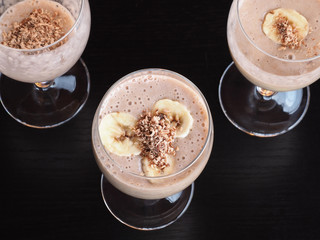 Three wine glasses with a milkshake, banana slices and chocolate closeup on a black background, top view. Natural homemade drink cocktail with fruit for proper nutrition.