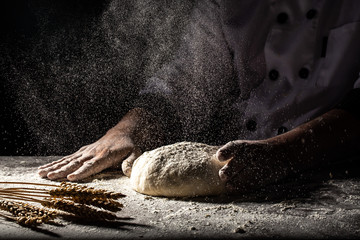 White flour flying into air as pastry chef in white suit slams ball dough on white powder covered...