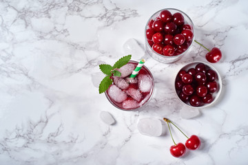 Fresh cherry lemonade with ice, mint and paper straw in sparkling glasses on table, copy space. Cold summer drink. Berry cocktail