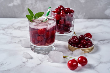 Fresh cherry lemonade with ice, mint and paper straw in sparkling glasses on table, copy space. Cold summer drink. Berry cocktail