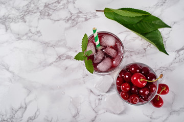 Fresh cherry lemonade with ice, mint and paper straw in sparkling glasses on table, copy space. Cold summer drink. Berry cocktail