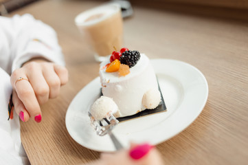 Young woman`s hands with a fork cutting off a piece or creamy parfait cake with raspberry and blackberry on top