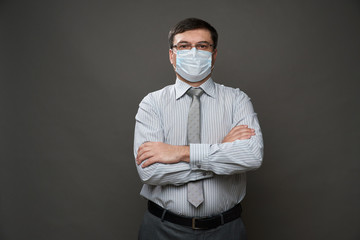 a man dressed as a businessman posing in a studio on a gray background, medical face mask, glasses, a light striped shirt and tie - casual office wear, concept of quarantine and antivirus protection