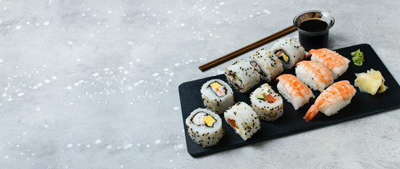 food delivery set of sushi and rolls with salmon and shrimp on a gray table next to a laptop. lunch...
