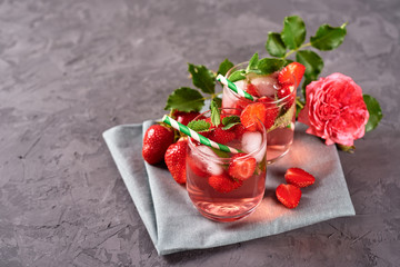 Fresh strawberry lemonade with ice, mint and paper straw in sparkling glasses on gray table background, copy space. Cold summer drink. Berry cocktail