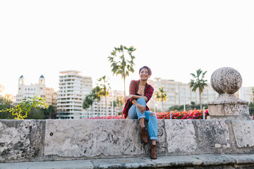 Fototapeta premium beautiful young woman happily staring at the camera outside on the street, sitting