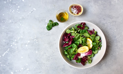 healthy diet salad from radicchio, arugula, valerian leaves with lemon and olive oil in a white bowl on a gray background. vitamin salad recipe. selective focus, copy space