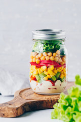 Fototapeta na wymiar Layering salad in a glass jar. Fresh radish, cucumber, celery, red bell pepper, corn, chickpeas and sauce.