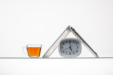 alarm clock under inverted laptop on inclined glass table surface isolated on white background  