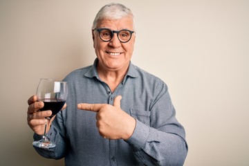 Senior handsome hoary man drinking glass of red wine over isolated white background very happy pointing with hand and finger
