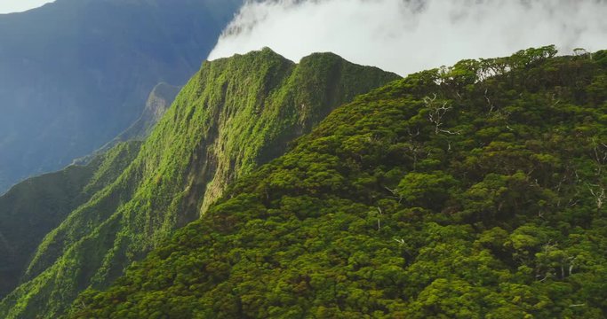Cinematic aerial view flying over lush green misty mountain peaks in Hawaii