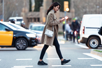 Pretty young woman crossing the street while listen to music with the wireless earphones.