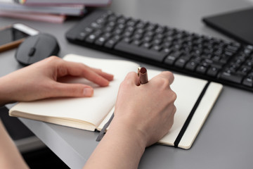 Female hand writing some date on in note at working space with keyboard and computer mouse at home  office.