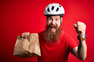 Redhead Irish delivery man with beard wearing bike helmet and holding takeaway paper bag screaming proud and celebrating victory and success very excited, cheering emotion