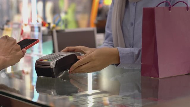 An upwardly mobile Asian Muslim man using a mobile phone to pay for a product at a sale terminal with nfc identification payment for verification and authentication