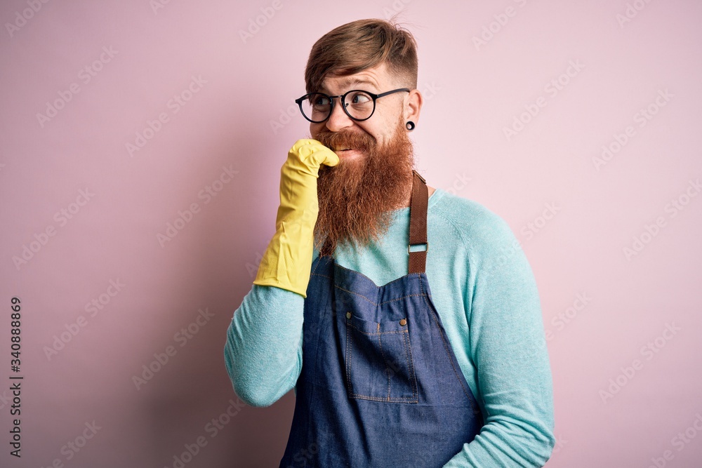 Sticker Irish redhead housekeeping man with beard wearing apron and washing gloves looking stressed and nervous with hands on mouth biting nails. Anxiety problem.