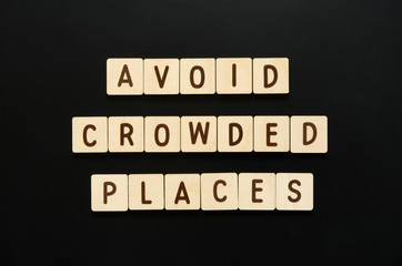 AVOID CROWDED PLACES - words from wooden blocks with letters. Top view on black background. - Image